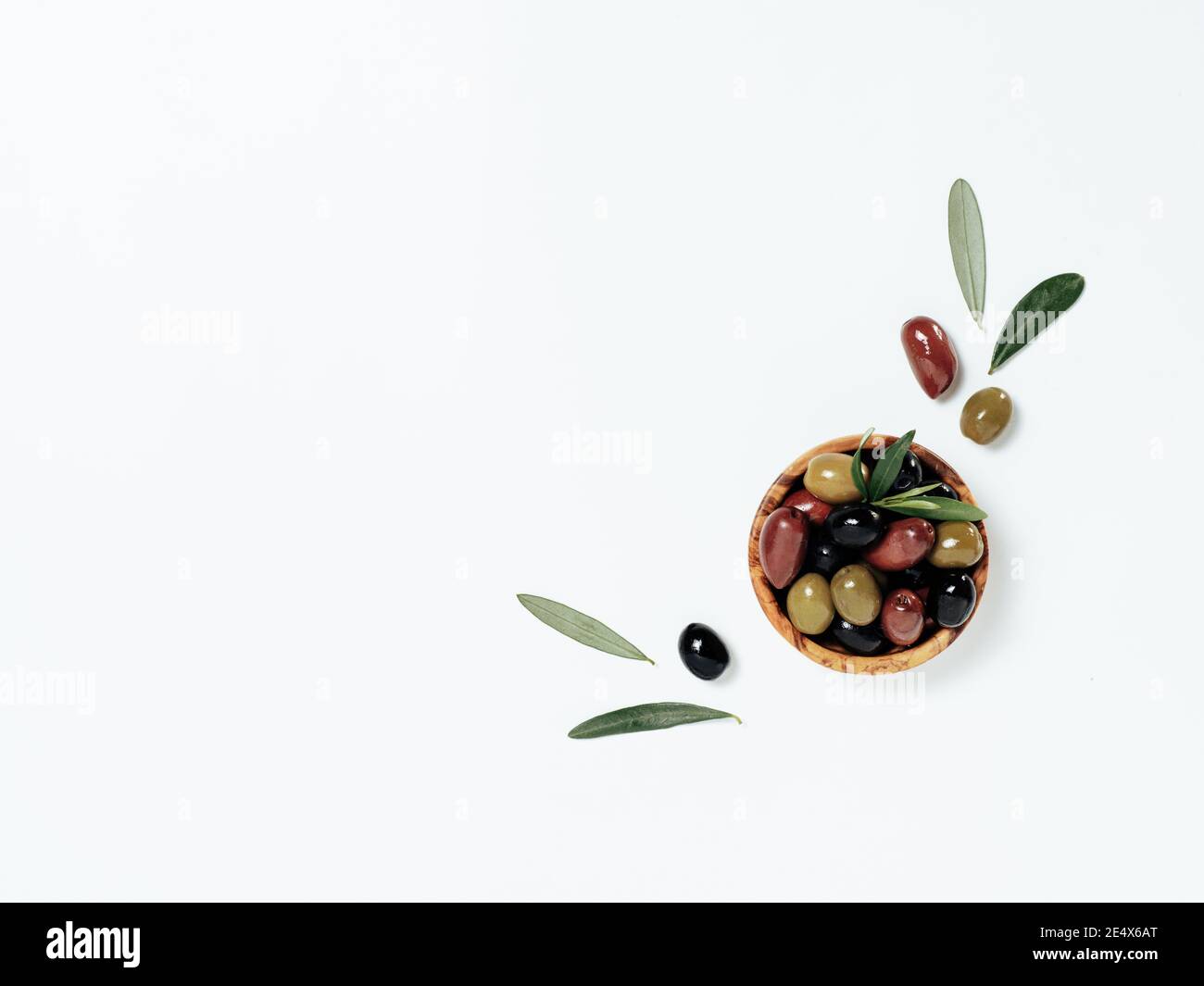 Olives tree leaves and fruits on white background. Small bowl with green, black and red kalamata olives, top view or flat lay. Olives isolated on white with copy space Stock Photo