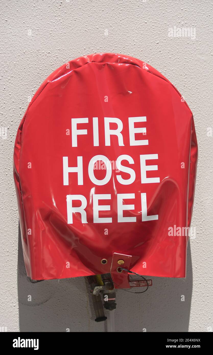 Fire Hose Reel covered by very bright shiny red cover with large white lettering. Emergency water supply mounted on exterior white wall.. Stock Photo