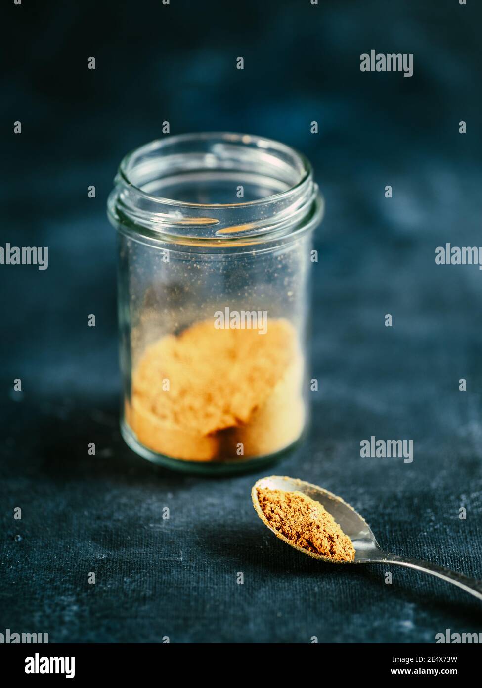 Indian or pakistani masala powder in spoon and glass jar. Homemade dry curry garam masala mix spices blend on dark gray and blue background. Vertical Stock Photo