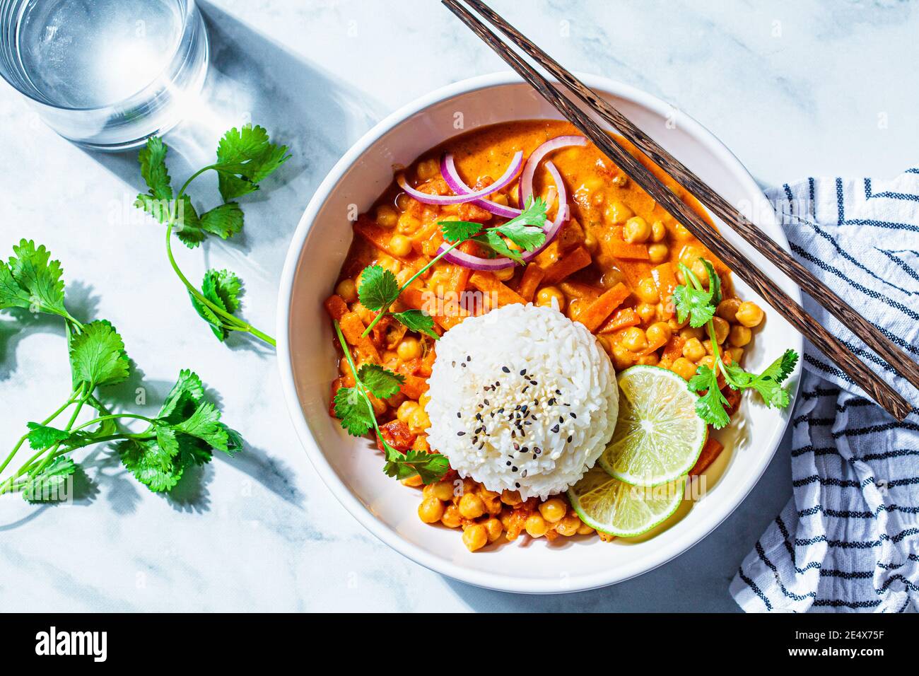 Vegan chickpea curry with rice and cilantro in a white bowl, white marble background. Indian