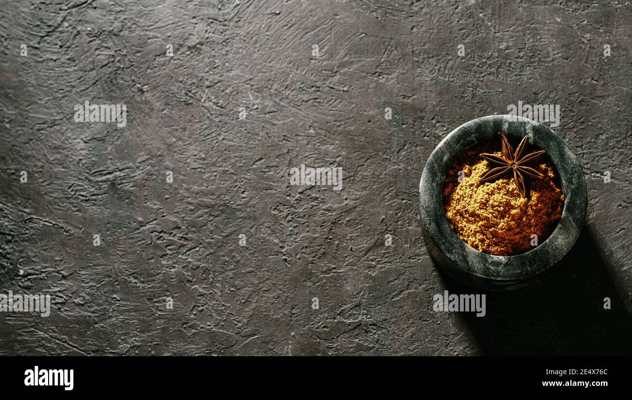 Indian or pakistani masala powder in black marble bowl on black textured background. Small marble bowl with dry curry garam masala mix spices blend with copy space. Top view or flat lay. Stock Photo