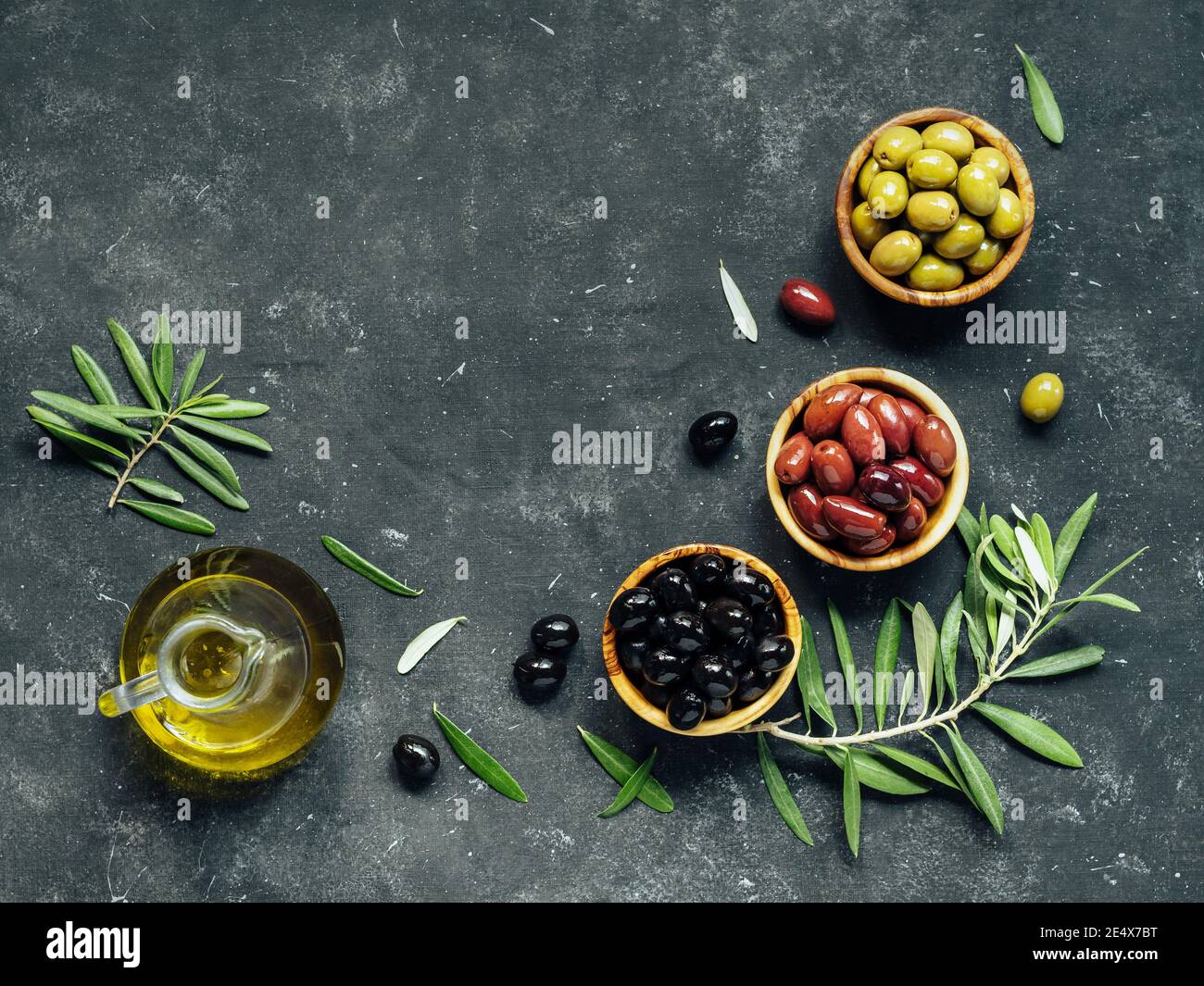 Set of green, black and red or pink olives and olive oil on dark background. Different types of olives in olive wooden bowls and olive oil over dark canvas background. Copy space. Top view or flat lay Stock Photo