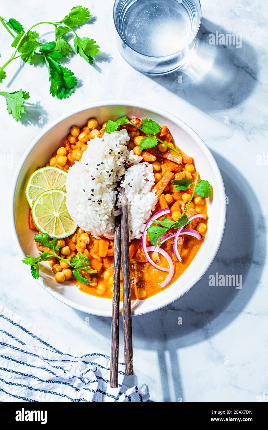 Vegan chickpea curry with rice and cilantro in a white bowl, white marble background. Indian