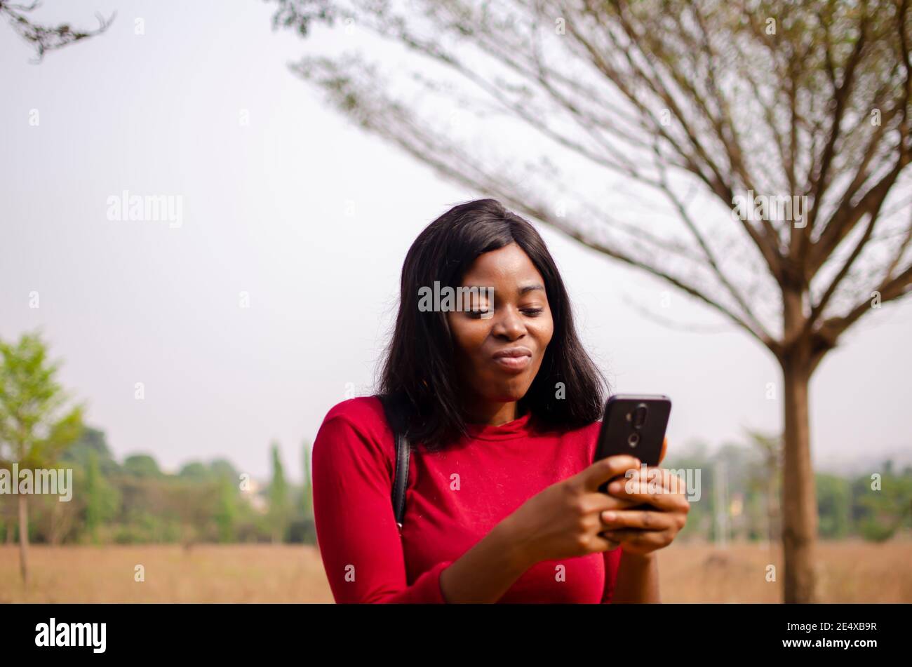 young black beautiful lady standing and using her smart phone in the park Stock Photo
