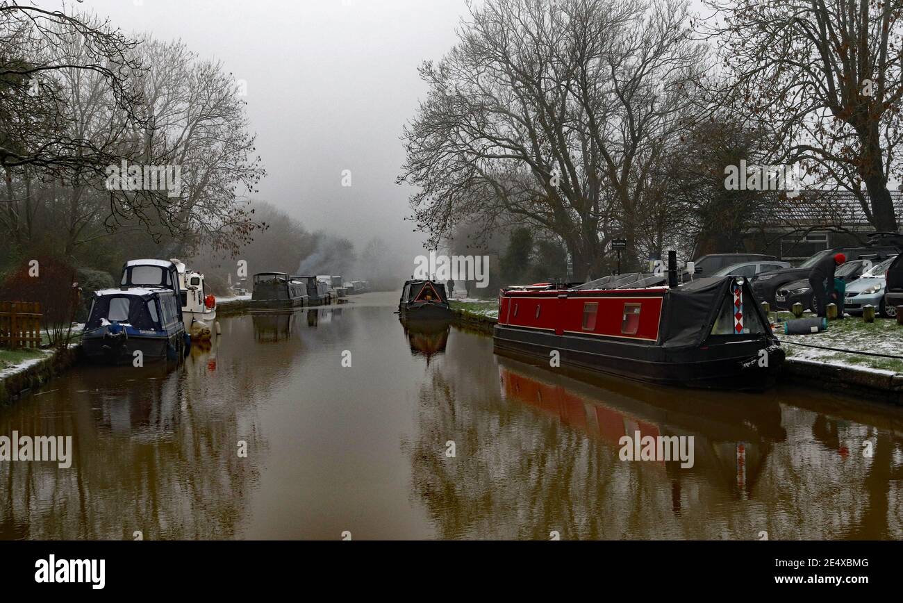 The waters of the canal in Parbold have partially frozen, while a red narrow boat provides a splash of colour on a misty, foggy and cold day Stock Photo