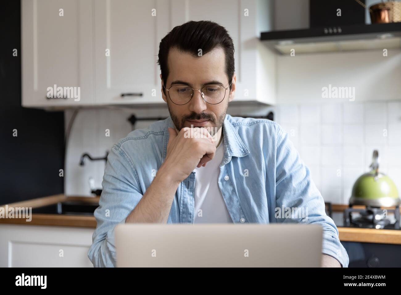 Doubtful man working from home pondering on data on screen Stock Photo