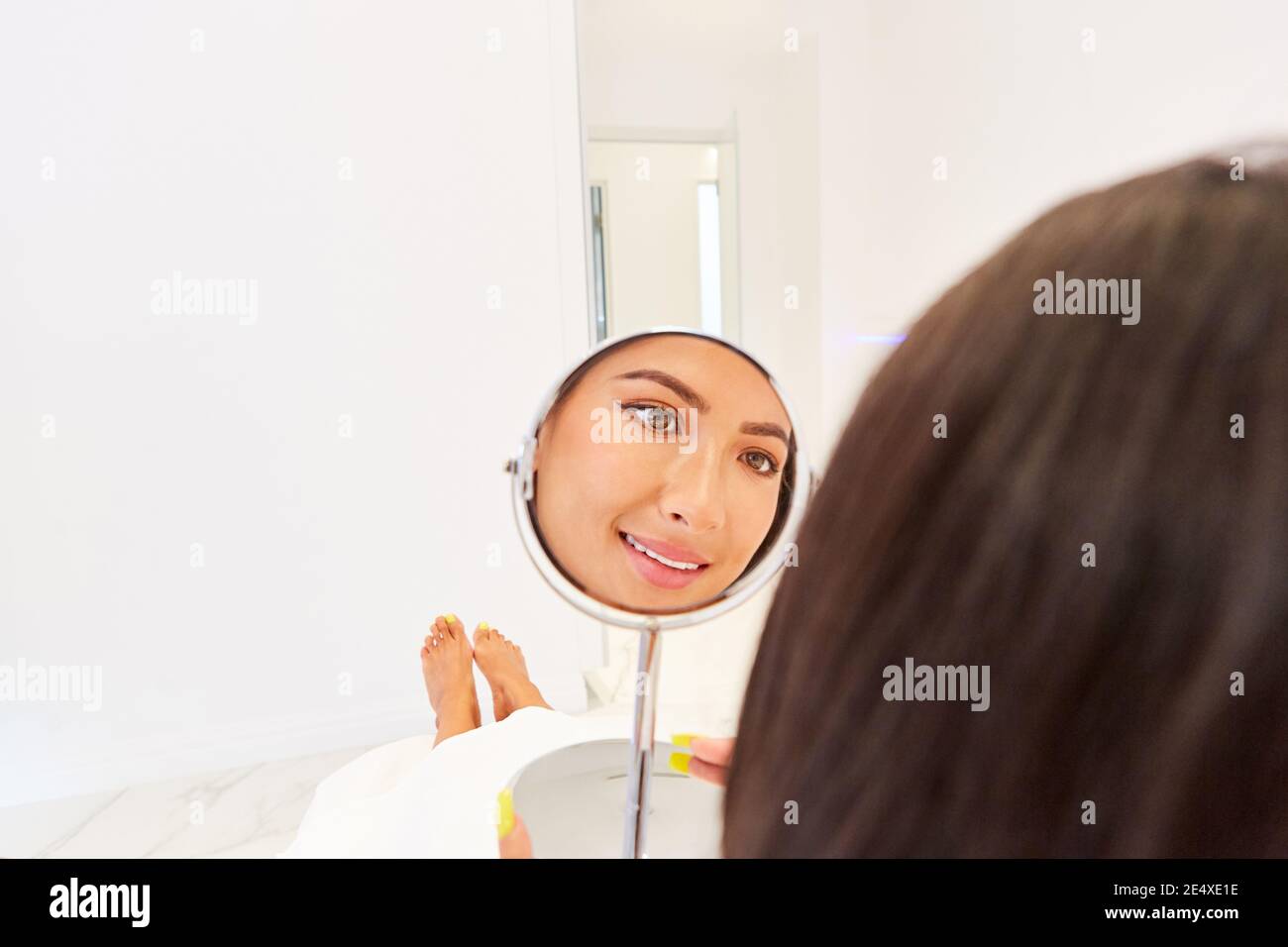 Young woman looks smiling in the mirror in the cosmetic studio or at the dermatologist Stock Photo