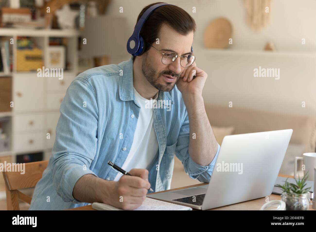 Young man getting remote education sitting by laptop in headphones Stock Photo