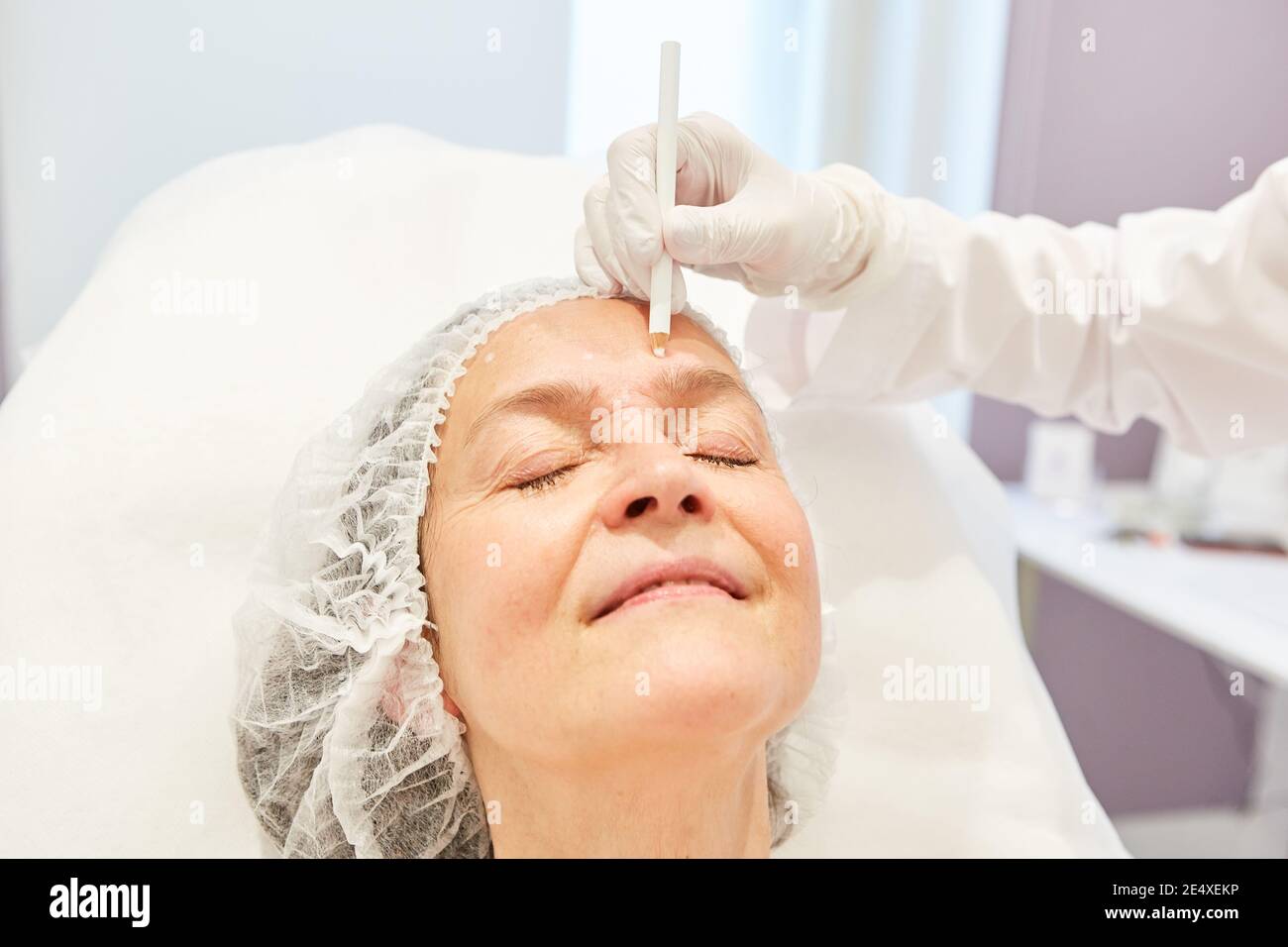 Elderly woman gets markings on her face for the facelift with hyaluronic acid dermal filler Stock Photo