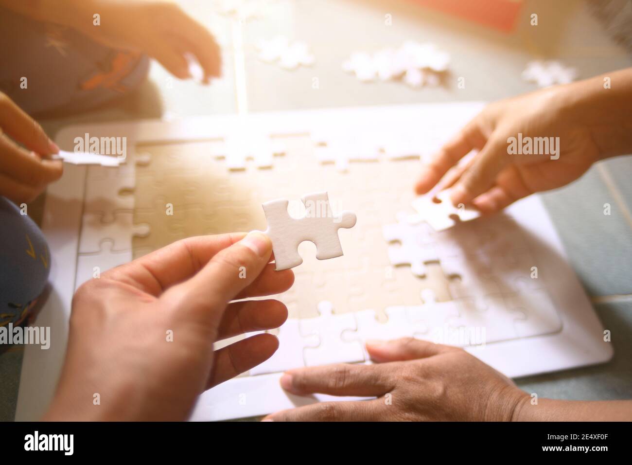 hand of father and little girl playing jigsaw puzzle for family concept shallow depth of field select focus on hands with sunlight affect Stock Photo