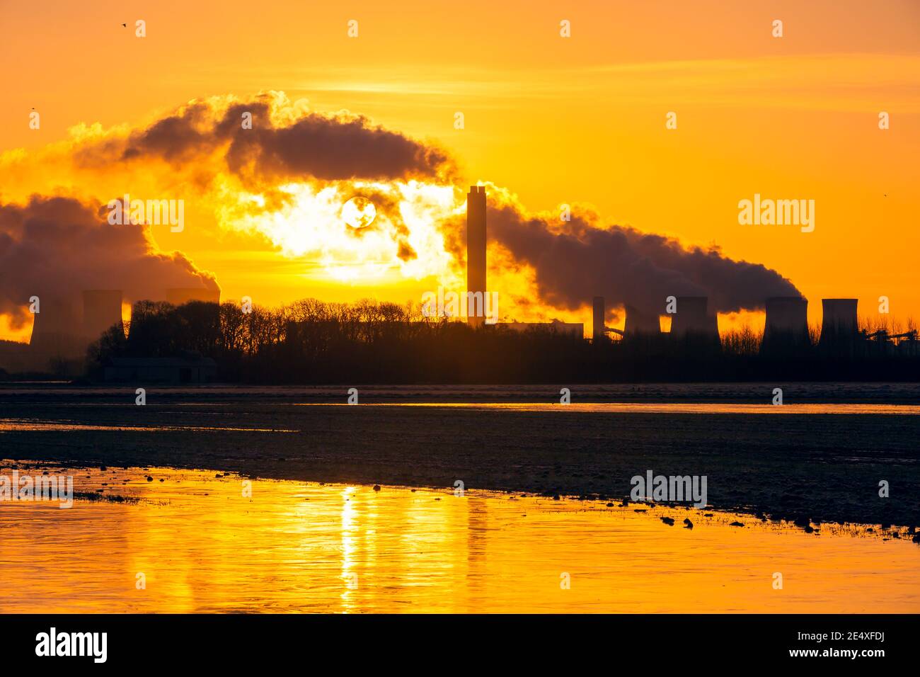 Sunrise in winter over Drax in North Yorkshire with the sun rising behind a water vapour trail from the cooling towers of a Power Plant.  Golden refle Stock Photo