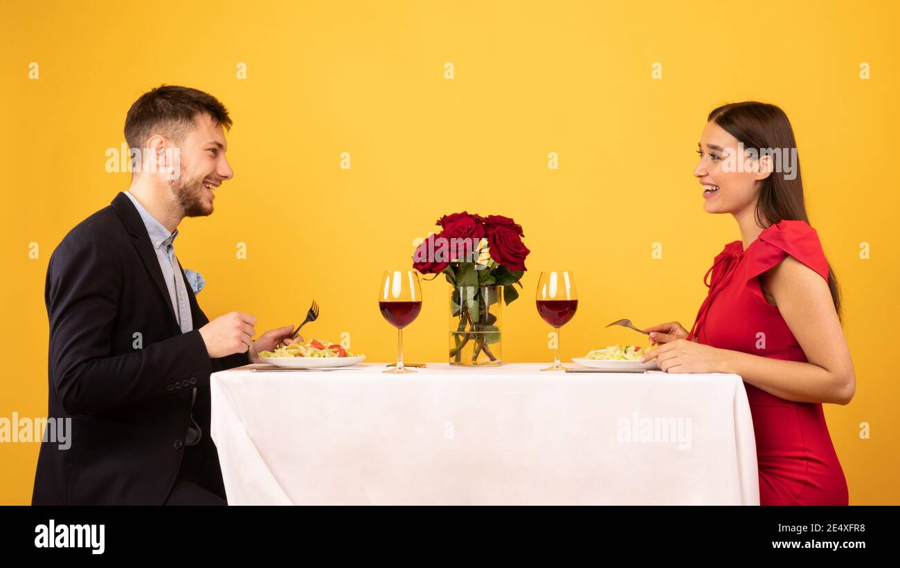 Happy Couple Talking Enjoying Dinner On Yellow Background, Studio Shot Stock Photo