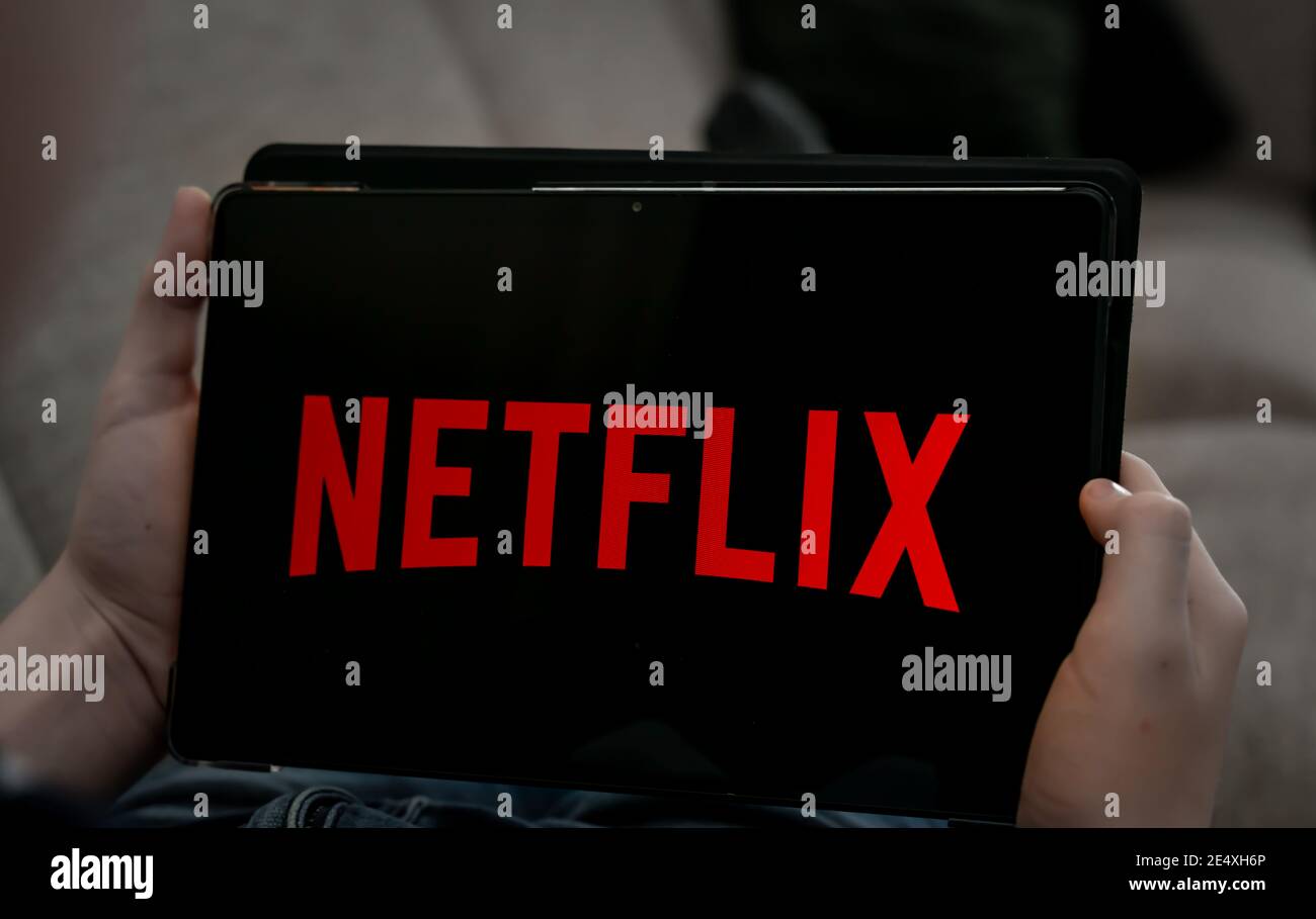 Hands holding tablet with Netflix logo on a black screen.  Stock Photo