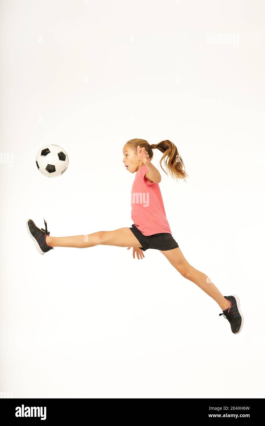 Cute female child football player looking at soccer ball and jumping in the air. Isolated on white background Stock Photo
