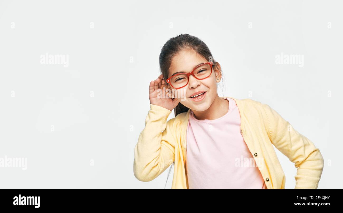 Child deafness concept. Cute mixed race little girl with a hand over her ear listening to sounds and voices, isolated on grey Stock Photo