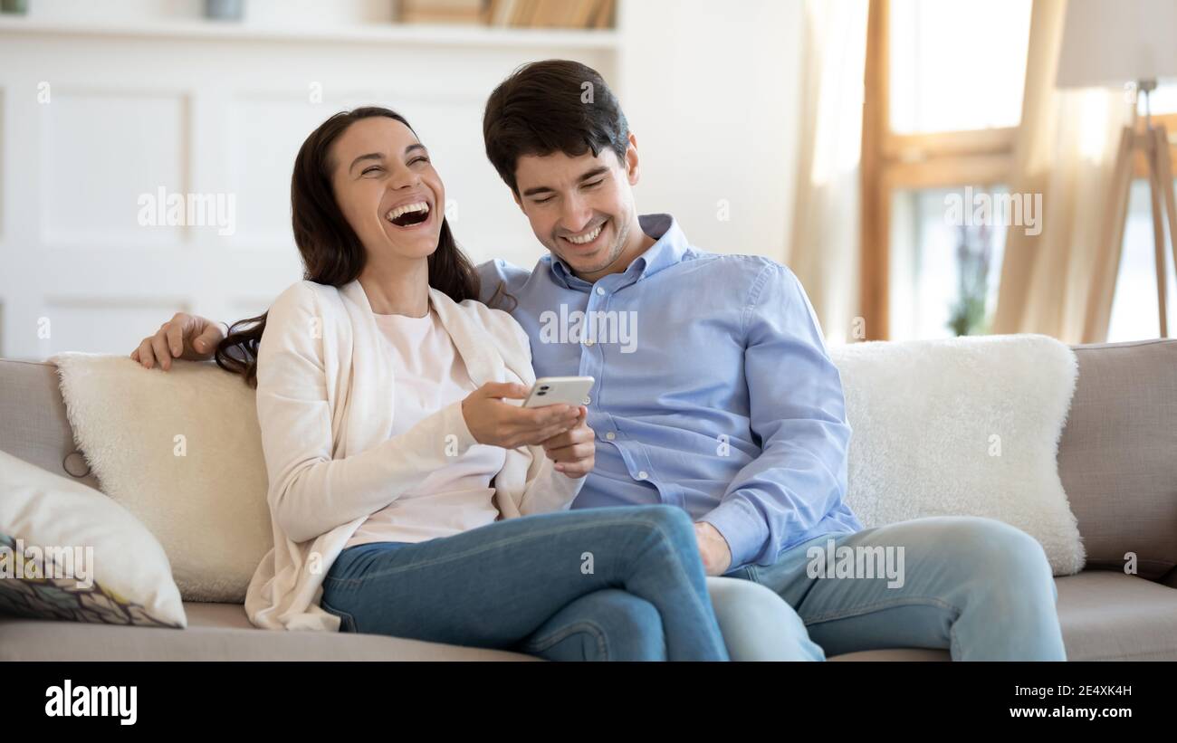 Happy young couple using phone, laughing, having fun together Stock Photo