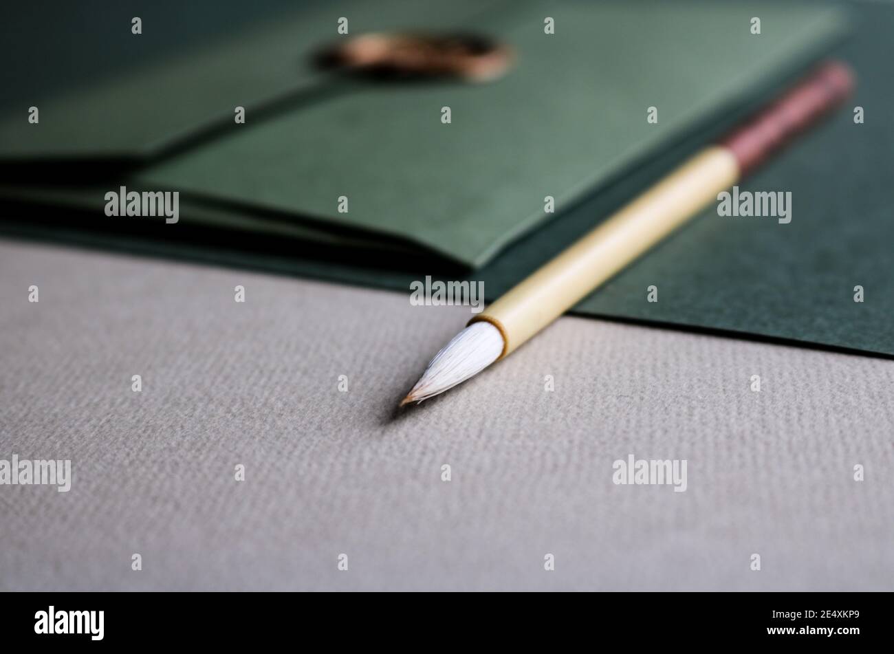 Close up of green coloured fine art paper, a green envelope with a golden seal and a wooden calligraphy brush laying on top of it Stock Photo