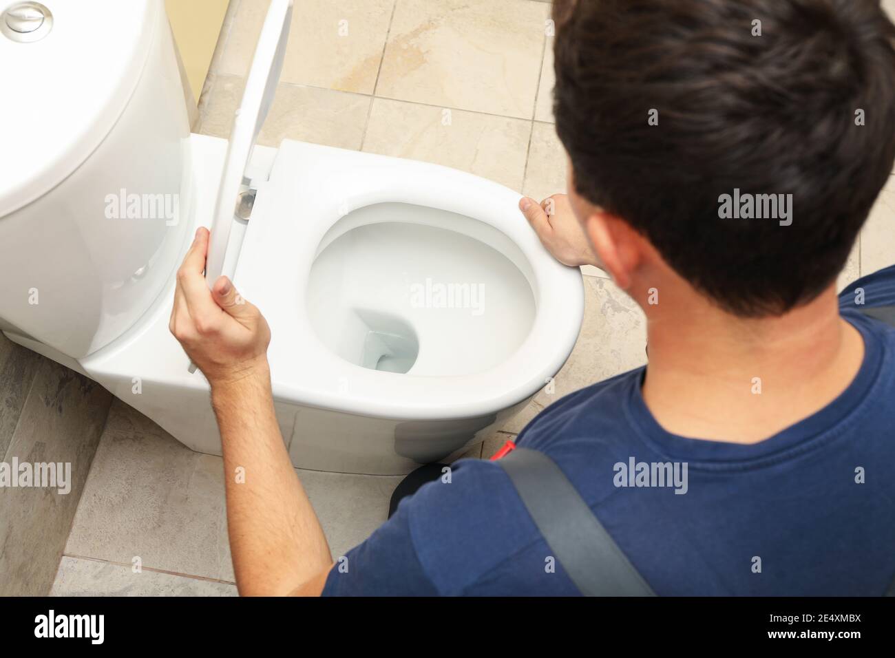 The plumber in overalls fixes the toilet Stock Photo Alamy