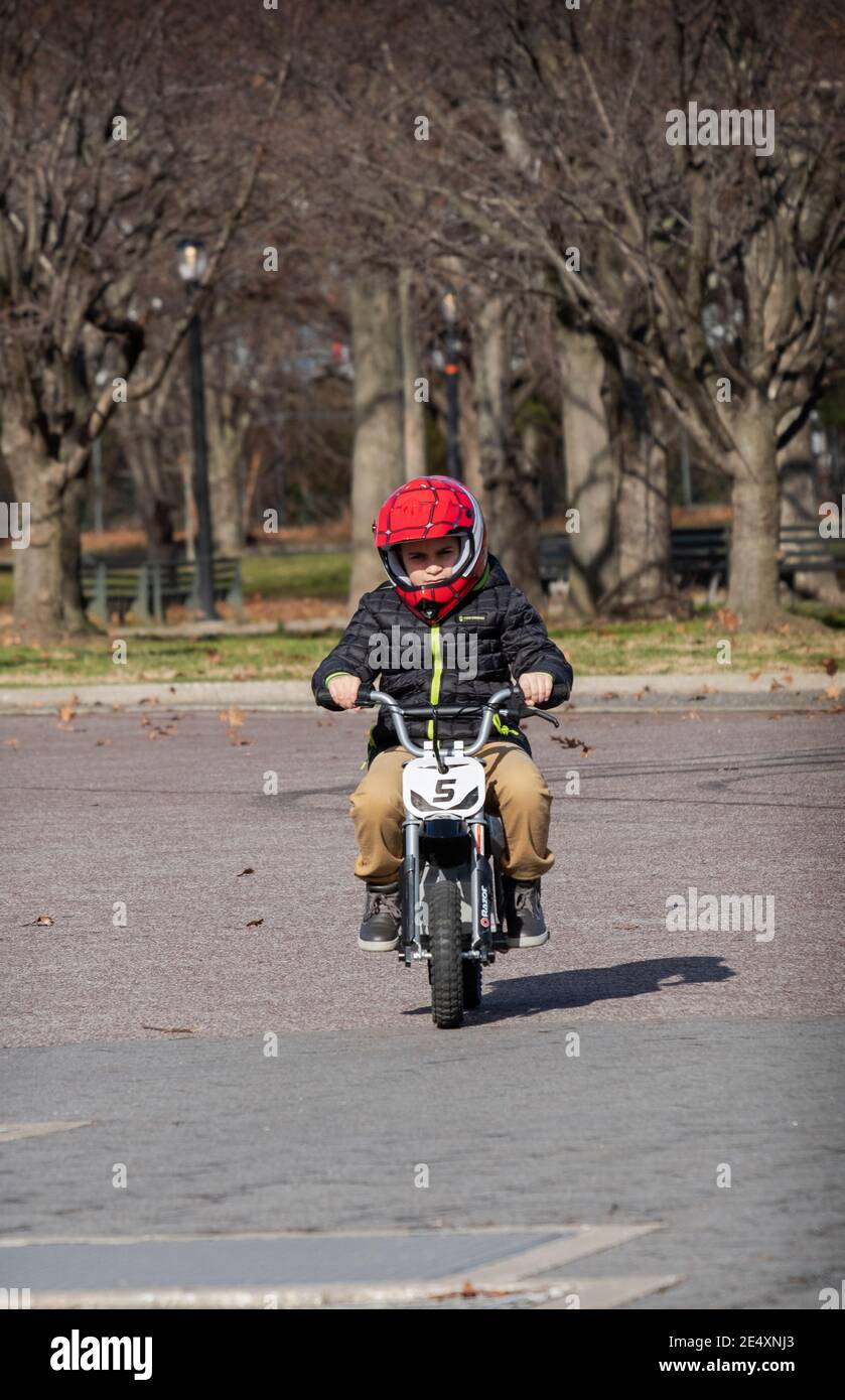 A young boy in a red helmet riding a Razor electric bicycle in a park in Queens, New York City. Stock Photo