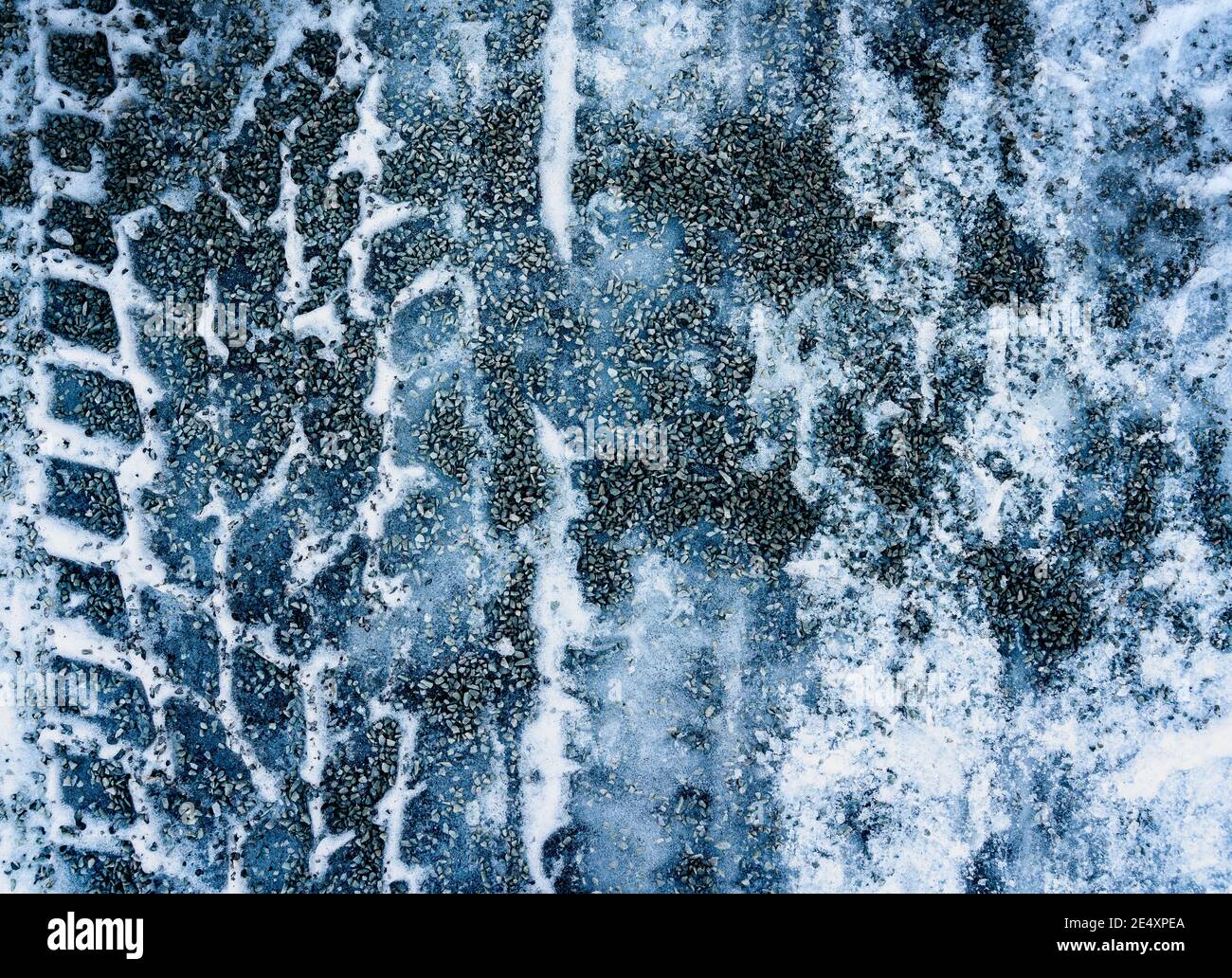 Close up of gravel strewn on an icy road with tire marks. Stock Photo