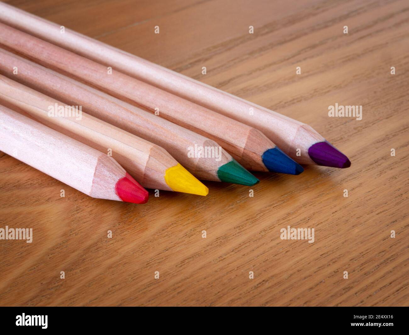 Five different colored pencils lines up on a wooden table Stock Photo