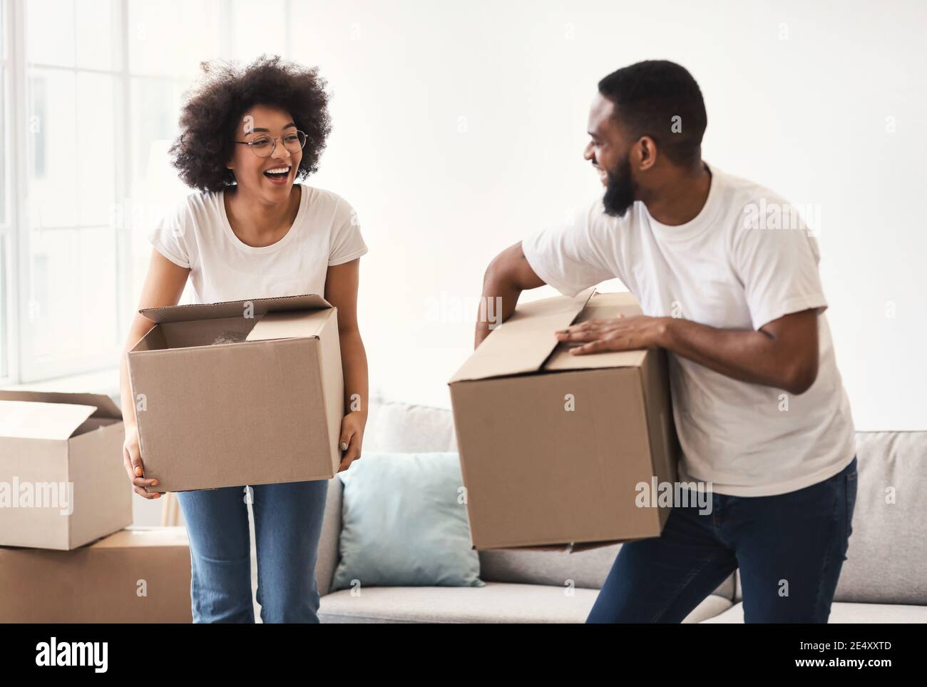 Happy African Couple Carrying Packed Moving Boxes Entering New Home Stock Photo
