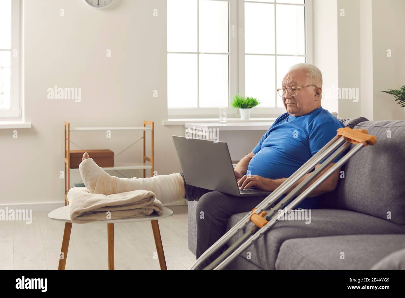 Serious senior man with broken leg in cast sitting on couch at home and