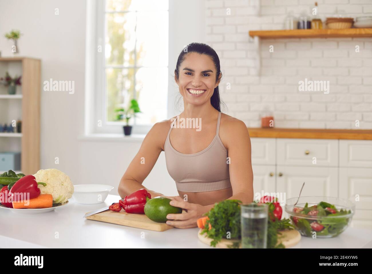 Happy cheerful sporty woman cooking a healthy vegetarian meal at the kitchen table Stock Photo
