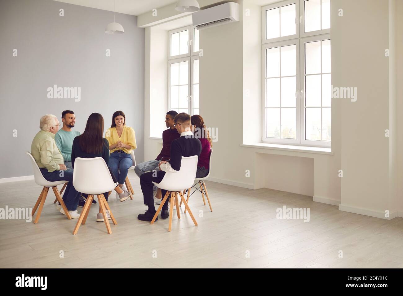 Diverse people sitting in circle and listening to friendly therapist in group therapy session Stock Photo