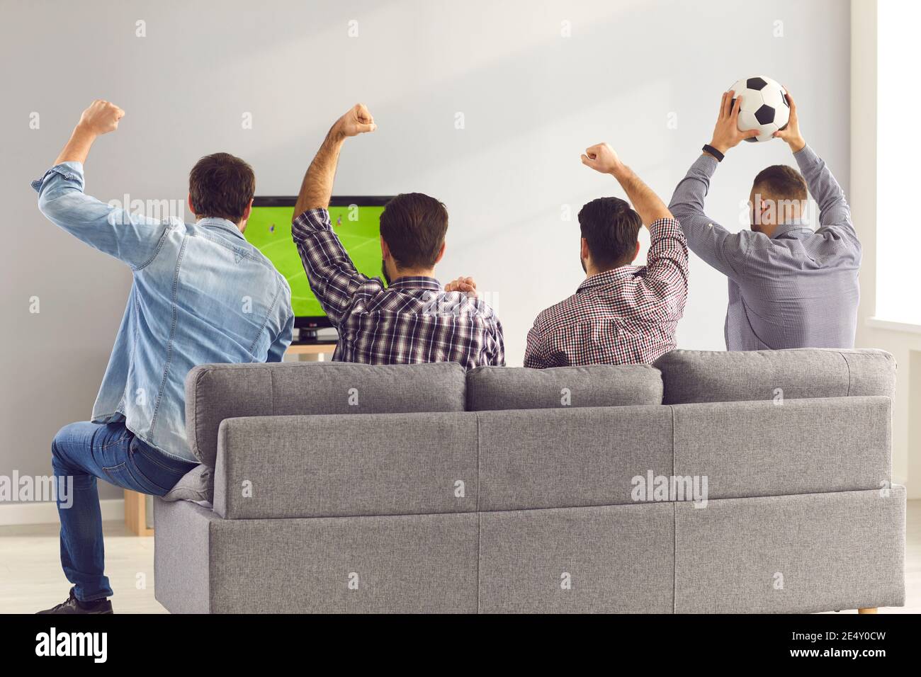 Four excited men friends sitting on sofa and watching emotionally soccer football match Stock Photo