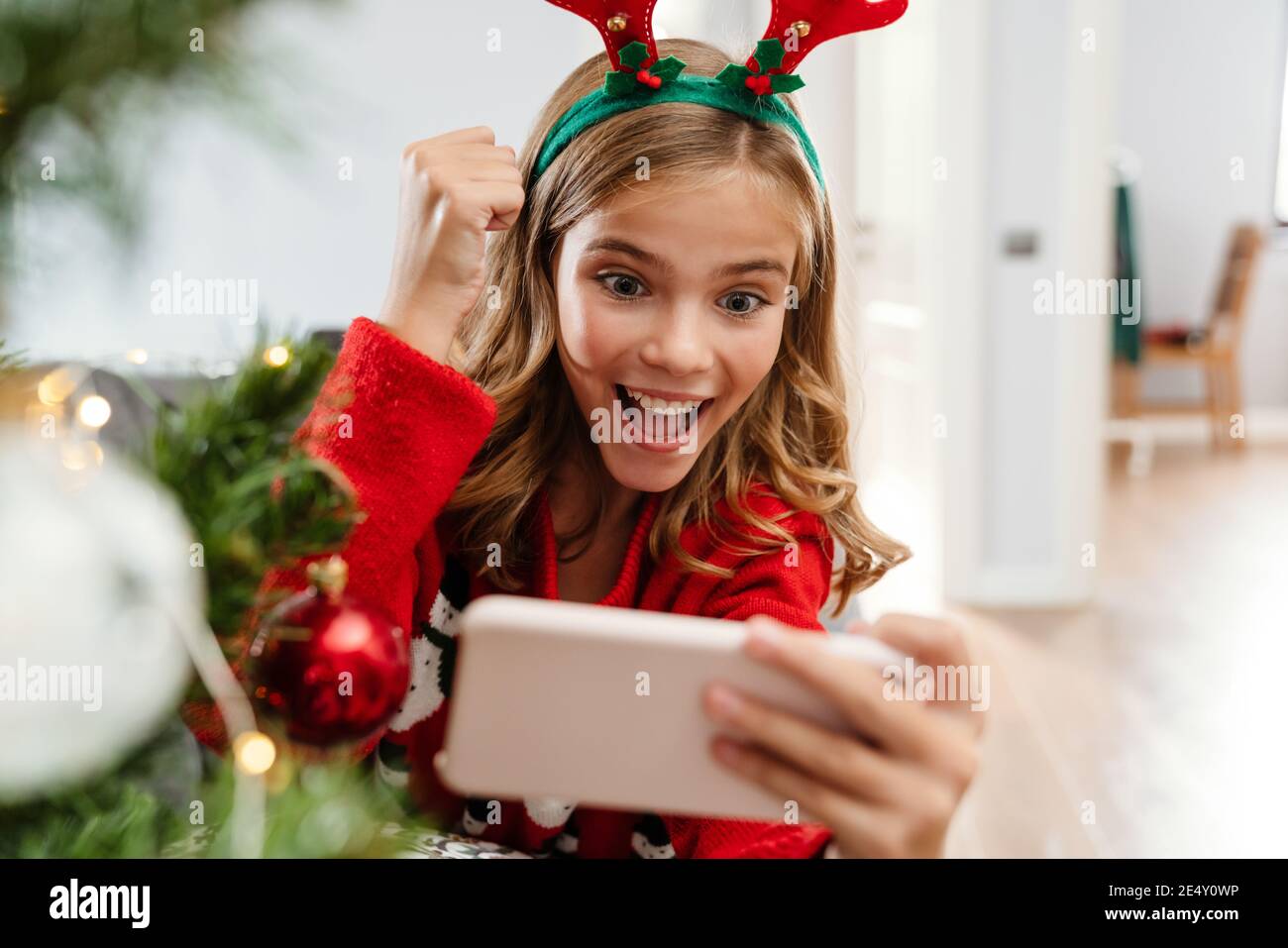 Excited caucasian girl making winner gesture while playing video game on cellphone at home Stock Photo