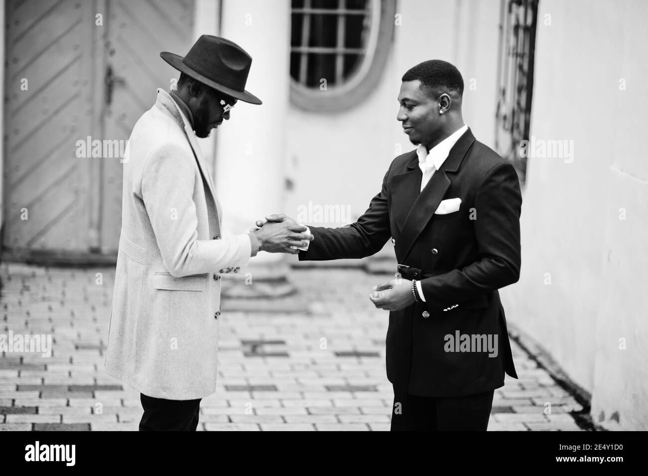 Two fashion black men shake hands each other. Fashionable portrait of african american male models. Wear suit, coat and hat. Stock Photo