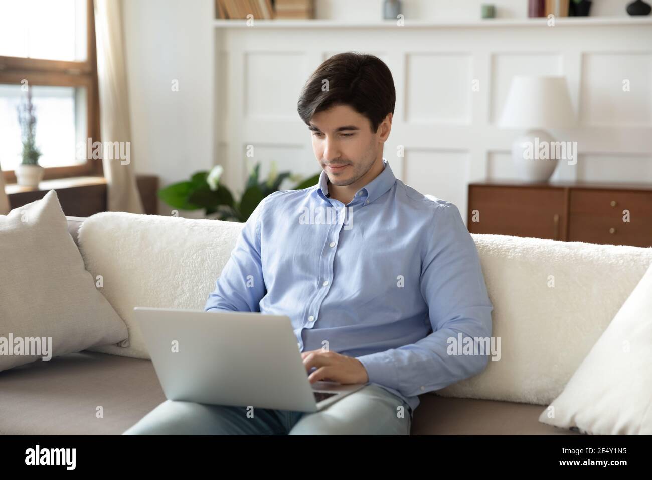 Focused man using laptop, sitting on couch at home Stock Photo