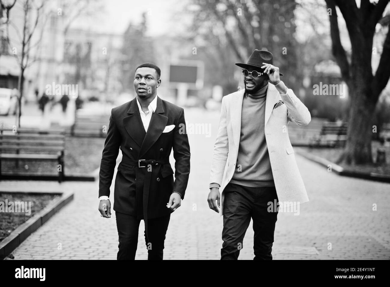 Two fashion black men walking on street. Fashionable portrait of african american male models. Wear suit, coat and hat. Stock Photo