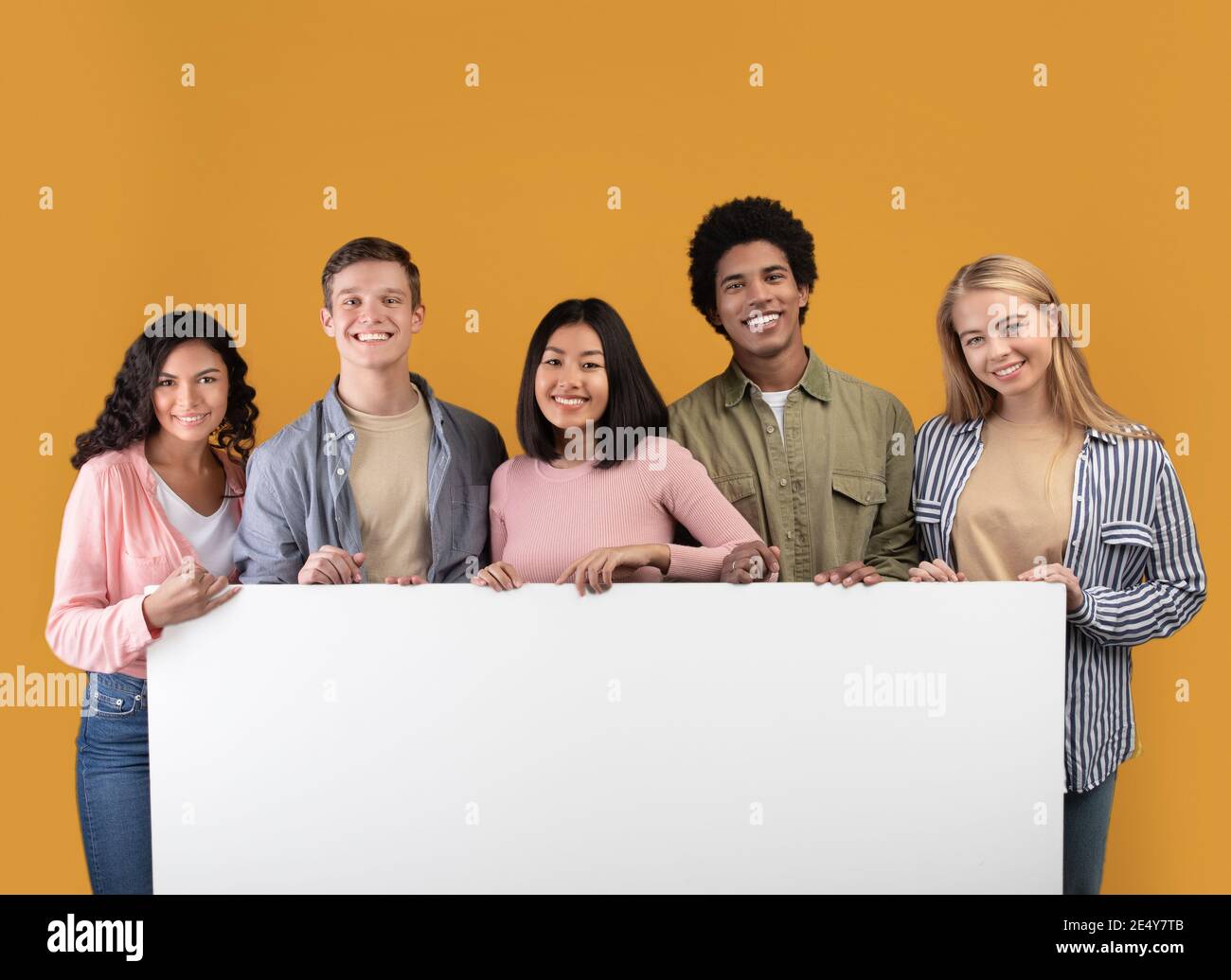 Diverse teens cheerful international students holding big banner with free space and ready to study Stock Photo