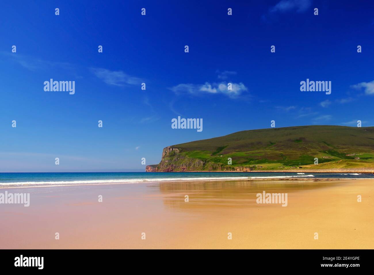 Sandy orange beach with green hills and cliffs in background, blue sky with white clouds on scottish island Hoy on Orkney summer day Stock Photo