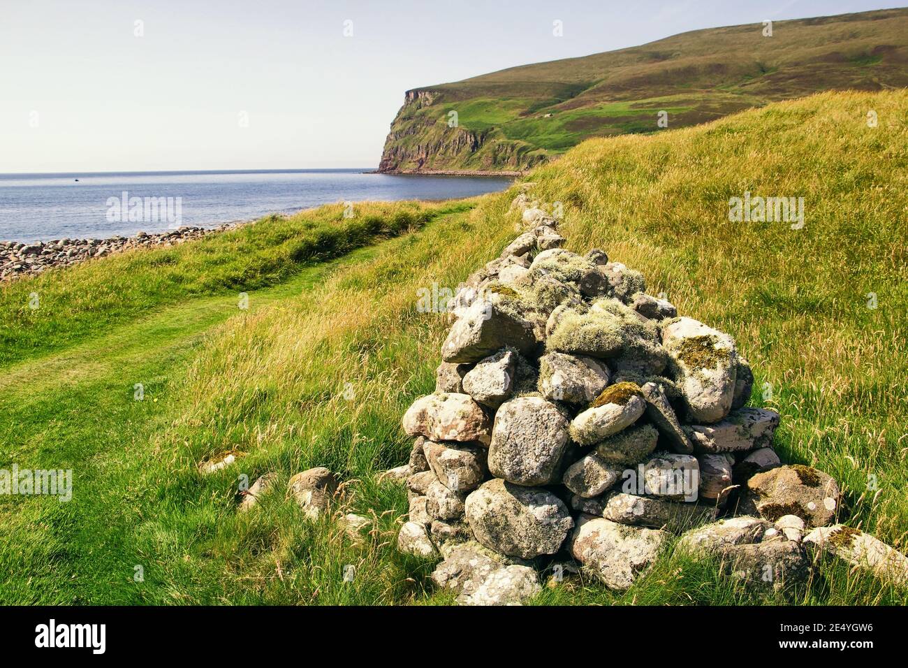 Drystone wall leading to green hills with blue ocean water on scottish islands shoreline on Orkney summer day Stock Photo