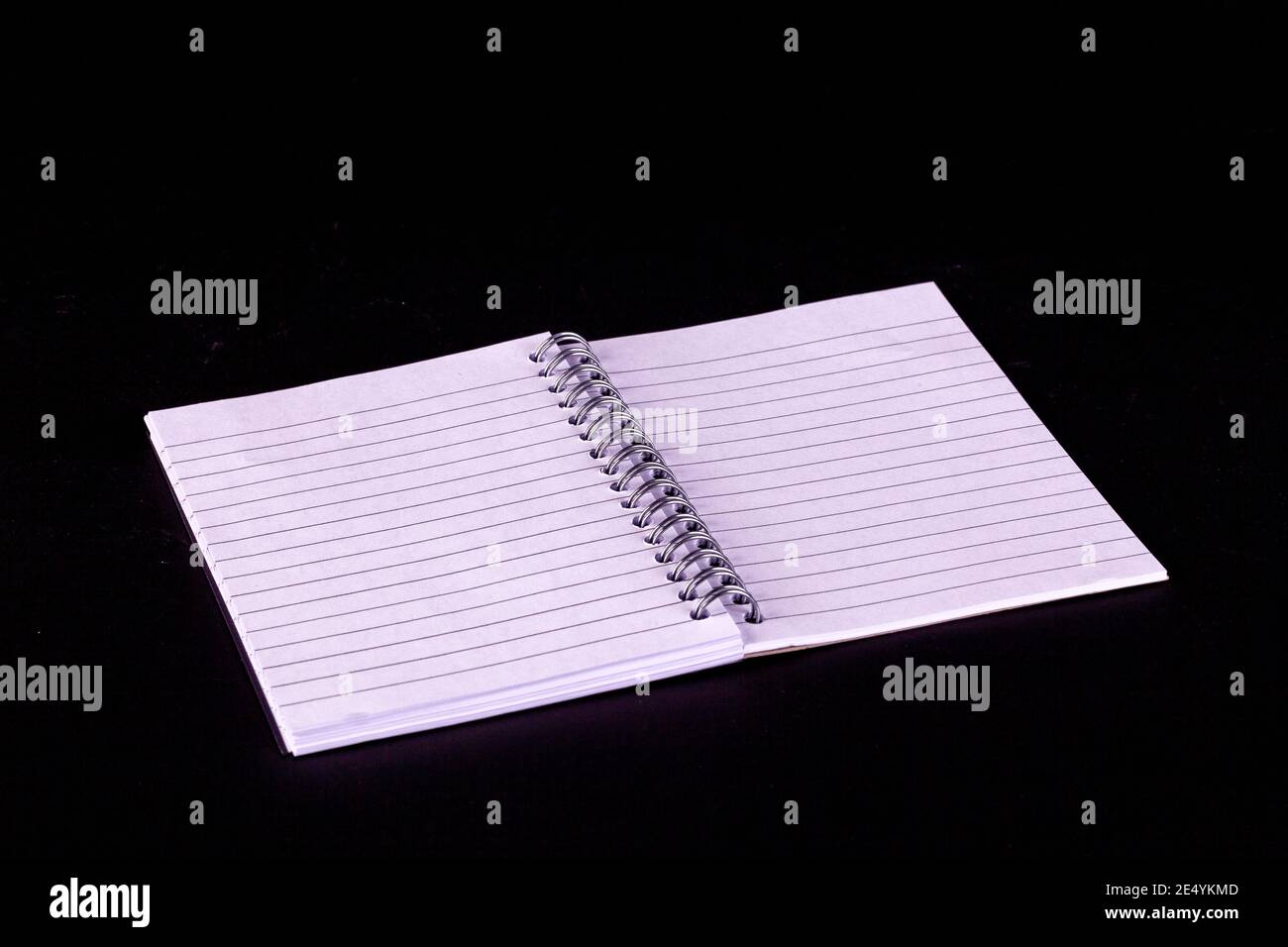 Opened A5 notepad with white lined pages and spiral boound with a black background Stock Photo
