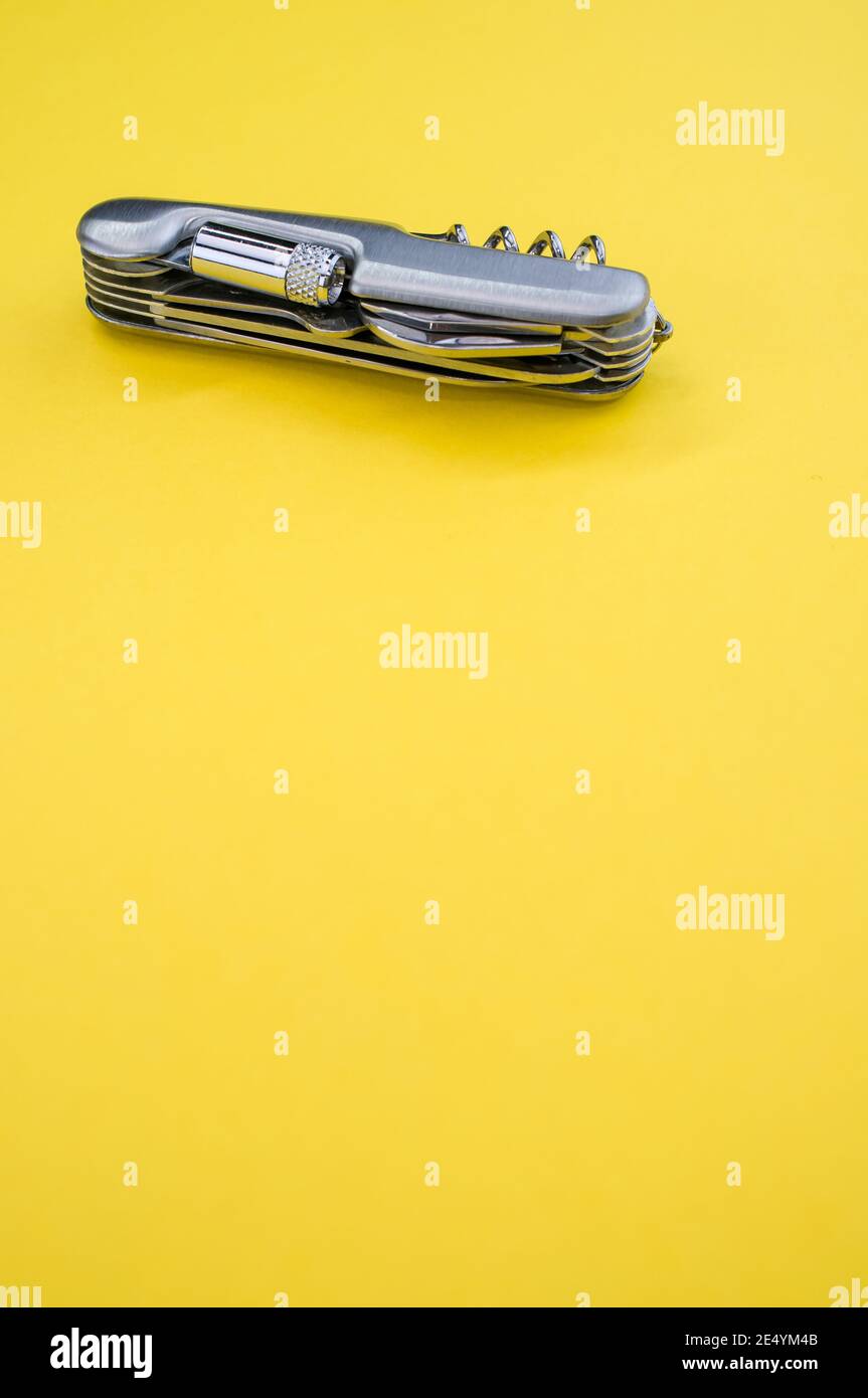 Vertical shot of a small folding pocket knife on a yellow surface under the lights Stock Photo