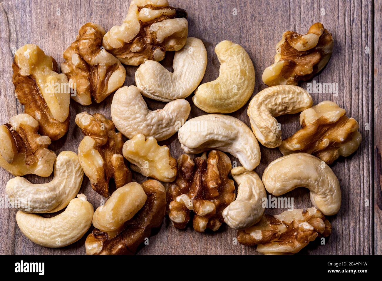 Raw cashews and walnut kernels lie, mixed in a bunch, on a wooden table Stock Photo