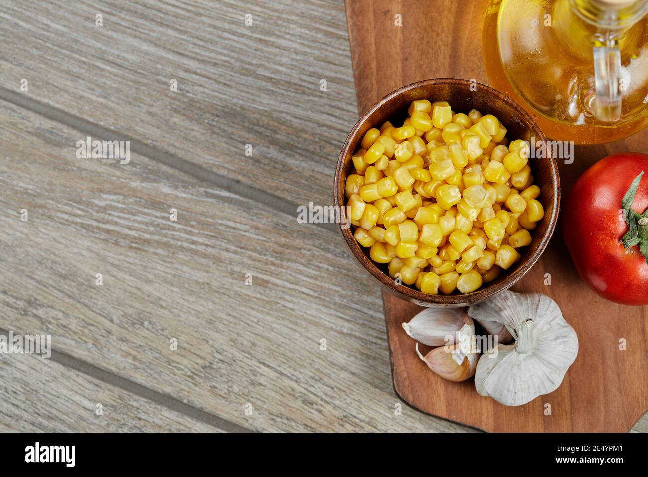 A bowl of boiled sweet corn, oil, and vegetables on a wooden board Stock Photo