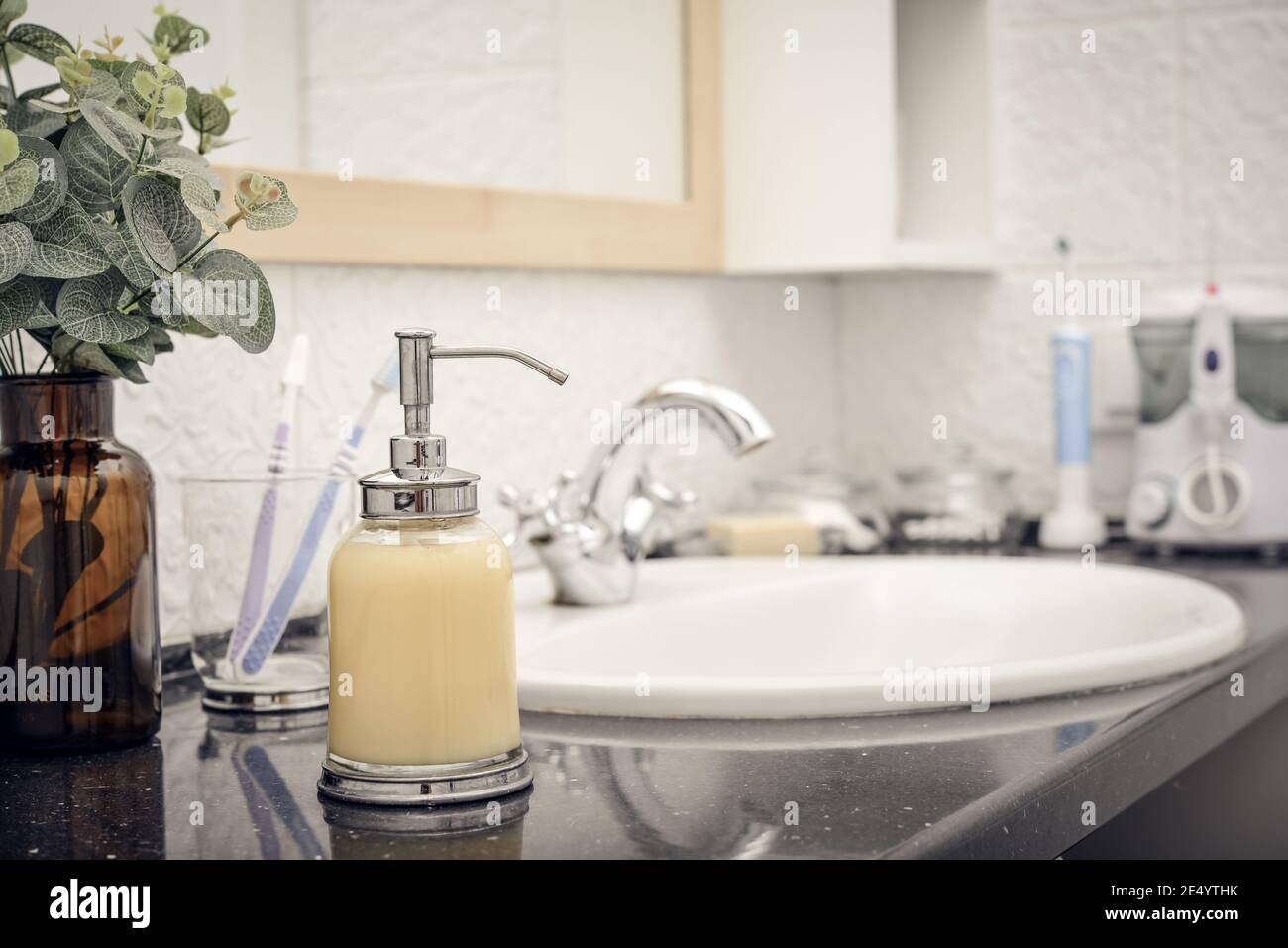 Bathroom sink and faucet with toothbrushes and soap dispenser Stock Photo -  Alamy