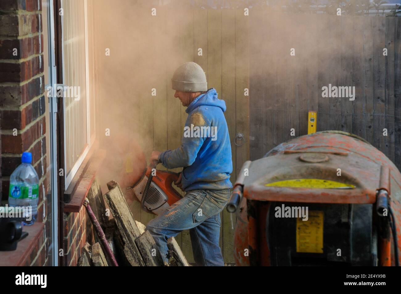 Building worker cutting through a brick wall with petrol masonry cutter and without protective gear. Stock Photo