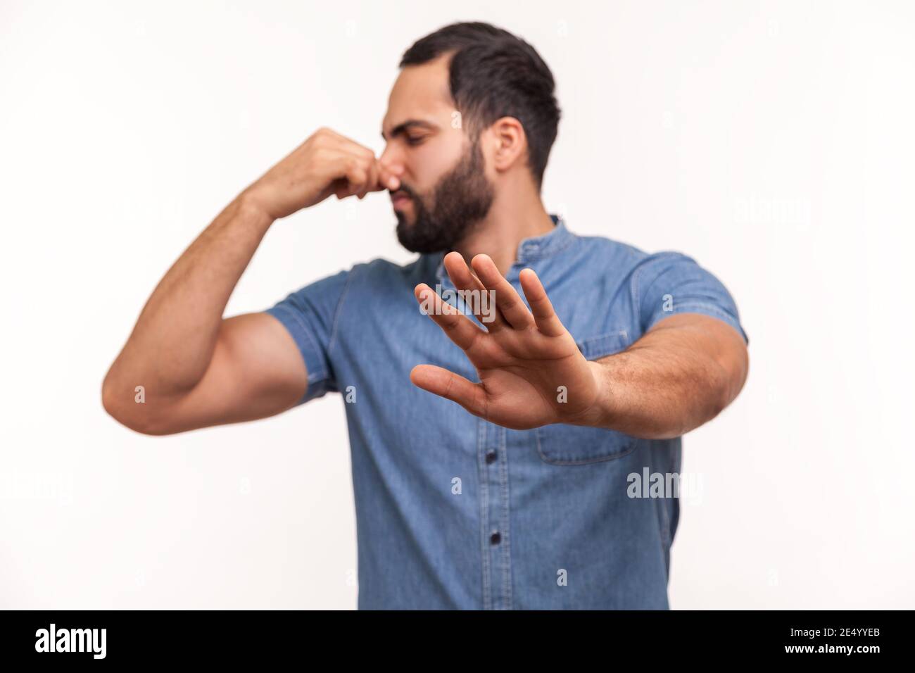 Confused unhappy bearded man grabbing nose with fingers and stretching hand out feeling disgusted unpleasant smell. Indoor studio shot isolated on whi Stock Photo