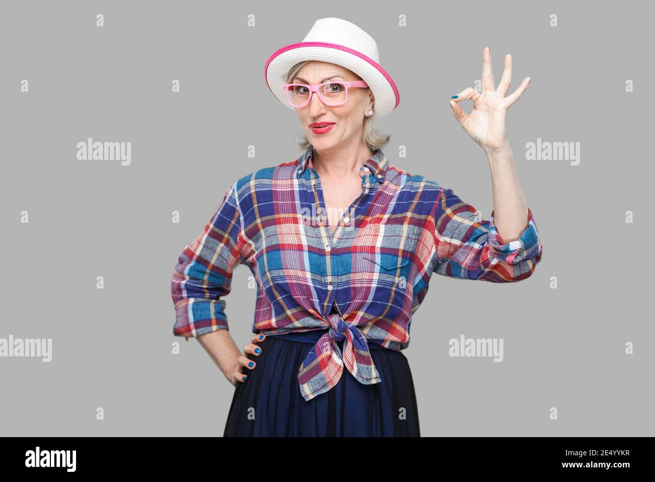 Portrait of funny happy modern cute stylish mature woman in casual style with hat and eyeglasses standing with Ok sign and looking at camera smiling. Stock Photo