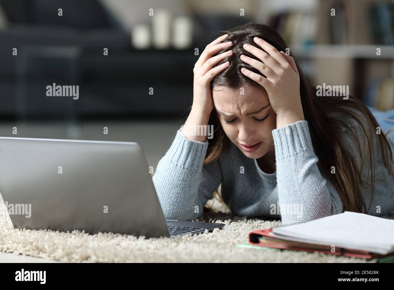 Sad student with laptop and notebook complaining lying on the floor in the night at home Stock Photo