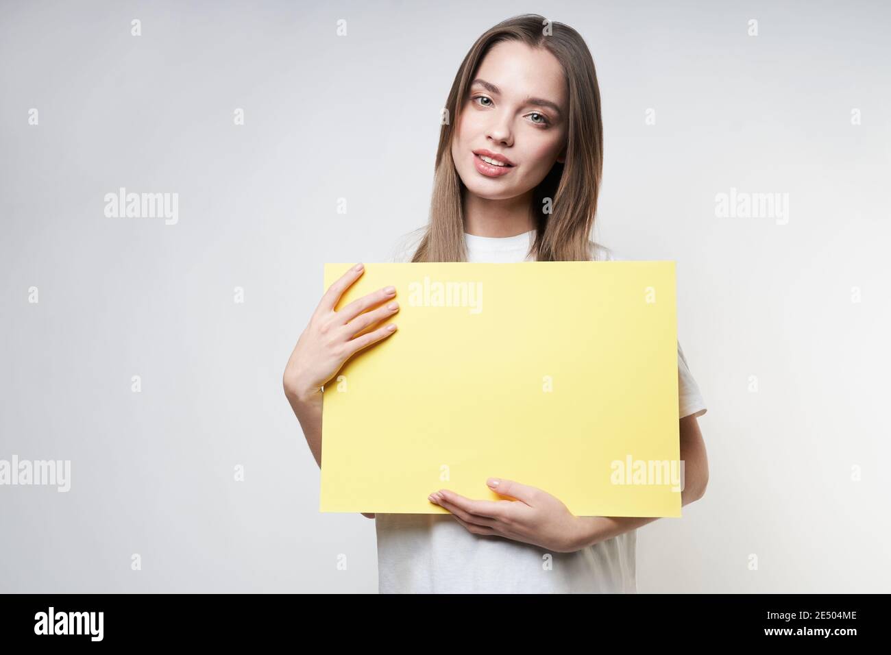 A beautiful blonde in a white T-shirt on a gray background holds a yellow sign. High quality photo Stock Photo