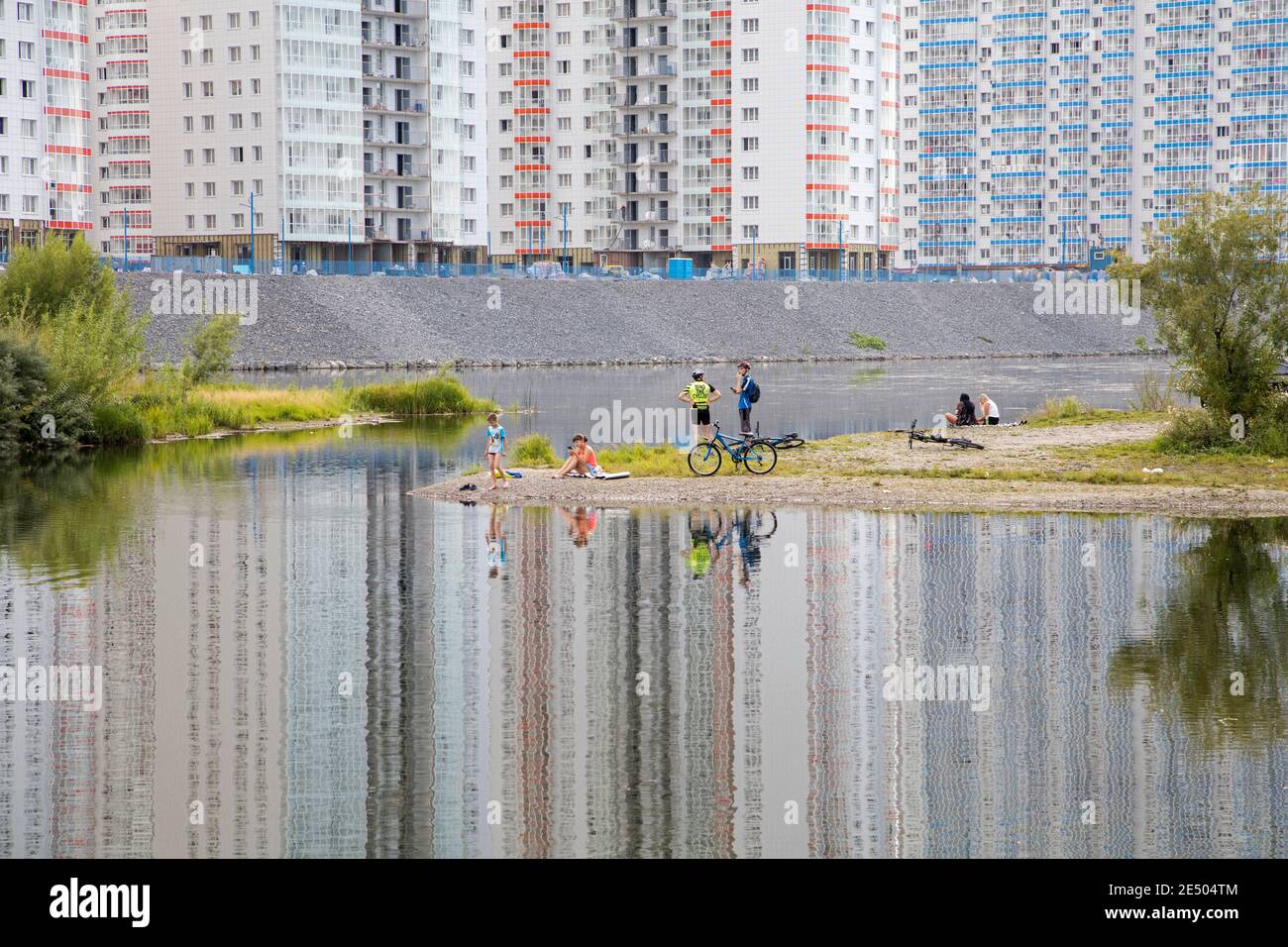 Local Russians relaxing on riverbank of the Yenisei River and newly built flats / apartments in suburb of city Krasnojarsk, Krasnoyarsk Krai, Russia Stock Photo
