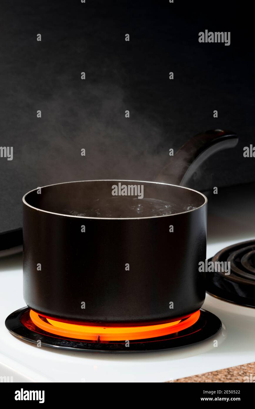 Vertical shot of water boiling in a black pot on a hot stove burner. Stock Photo