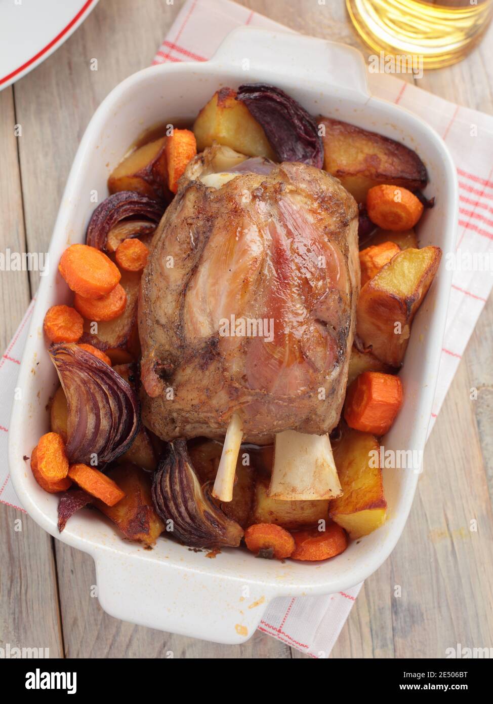 Traditional German dish Eisbein, the roasted pork knuckle with roasted potato, carrot, and onion on a rustic table Stock Photo